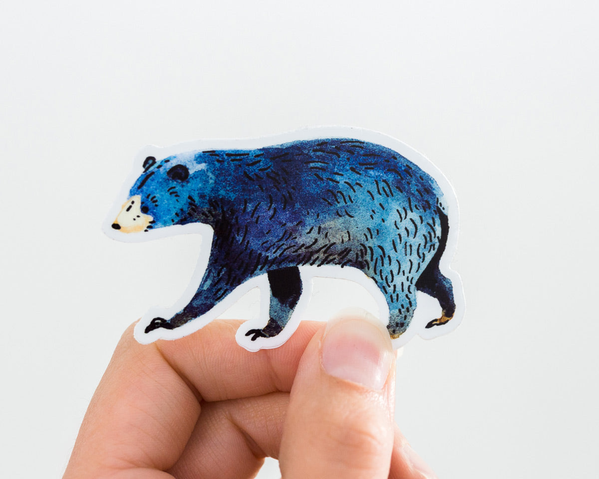 a hand holding a cute black bear vinyl sticker by wildship studio