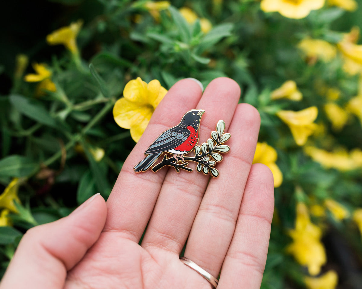 robin enamel pin held in hand with yellow flowers