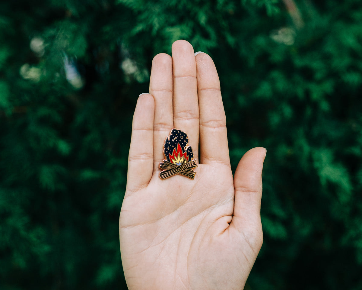 michigan campfire enamel pin held in palm of a hand