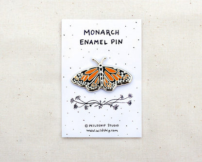 a gold enamel lapel pin of an orange and black monarch butterfly pinned to a backing card