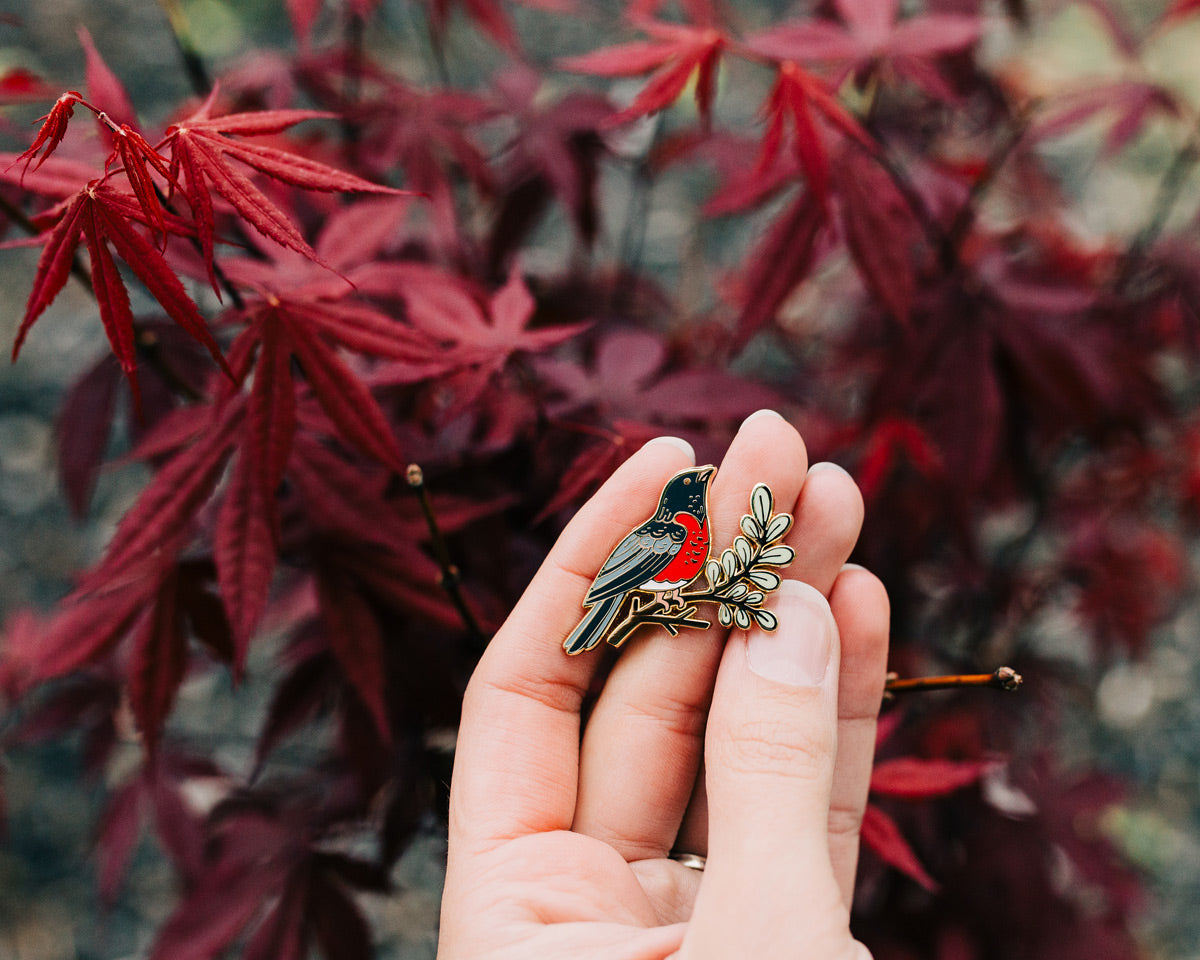 robin enamel pin being held in hand outdoors