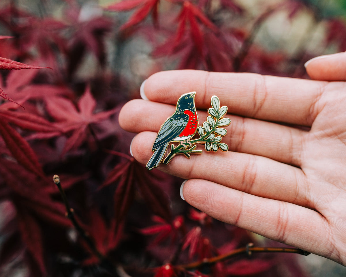 robin enamel pin held in hand against red leaves