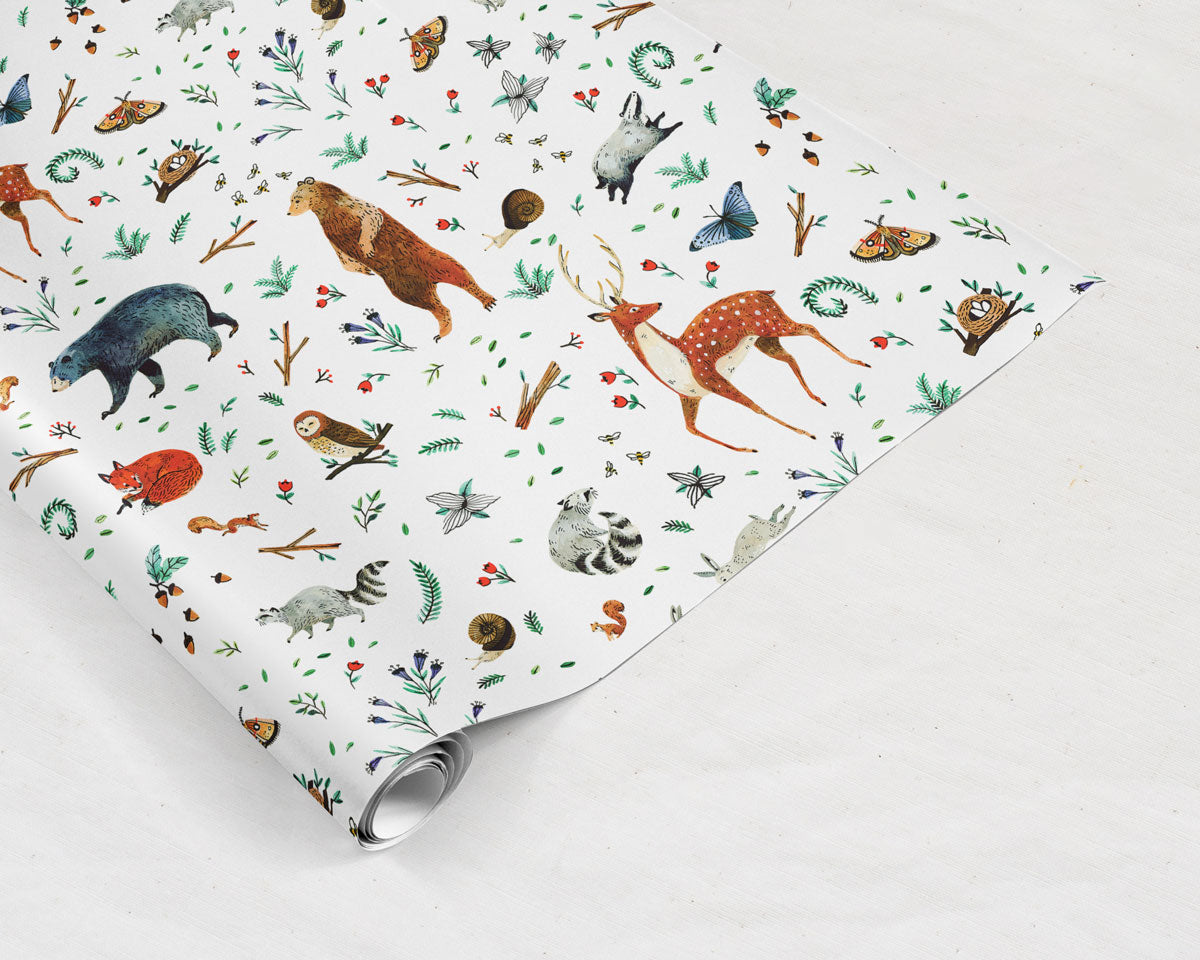 partially unrolled preview of Wildship Studio gift wrapping paper with woodland deer, bears, raccoons, butterflies, foxes, and other animals and flowers