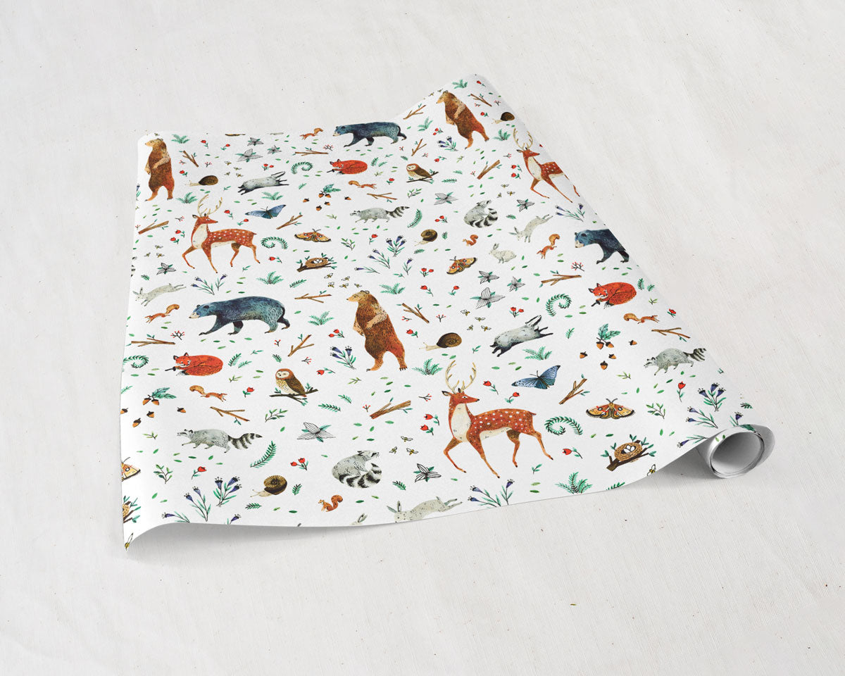 partially unrolled sheets of Wildship Studio gift wrapping paper with woodland deer, bears, raccoons, butterflies, foxes, and other animals and flowers