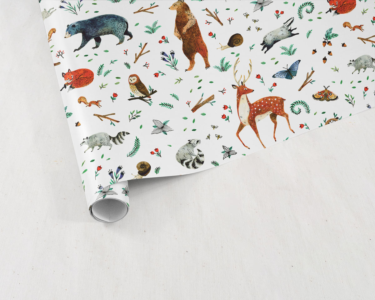 partially unrolled sheet of Wildship Studio gift wrapping paper with woodland deer, bears, raccoons, butterflies, foxes, and other animals and flowers