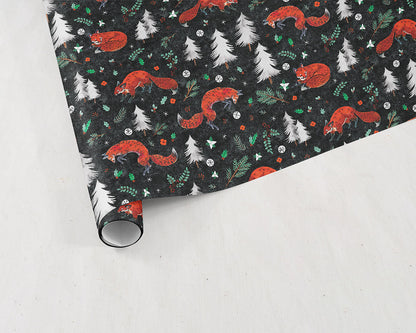 partially unrolled sheet of Wildship Studio holiday gift wrapping paper with fox, pine trees, snowflakes, poinsettia, and holly